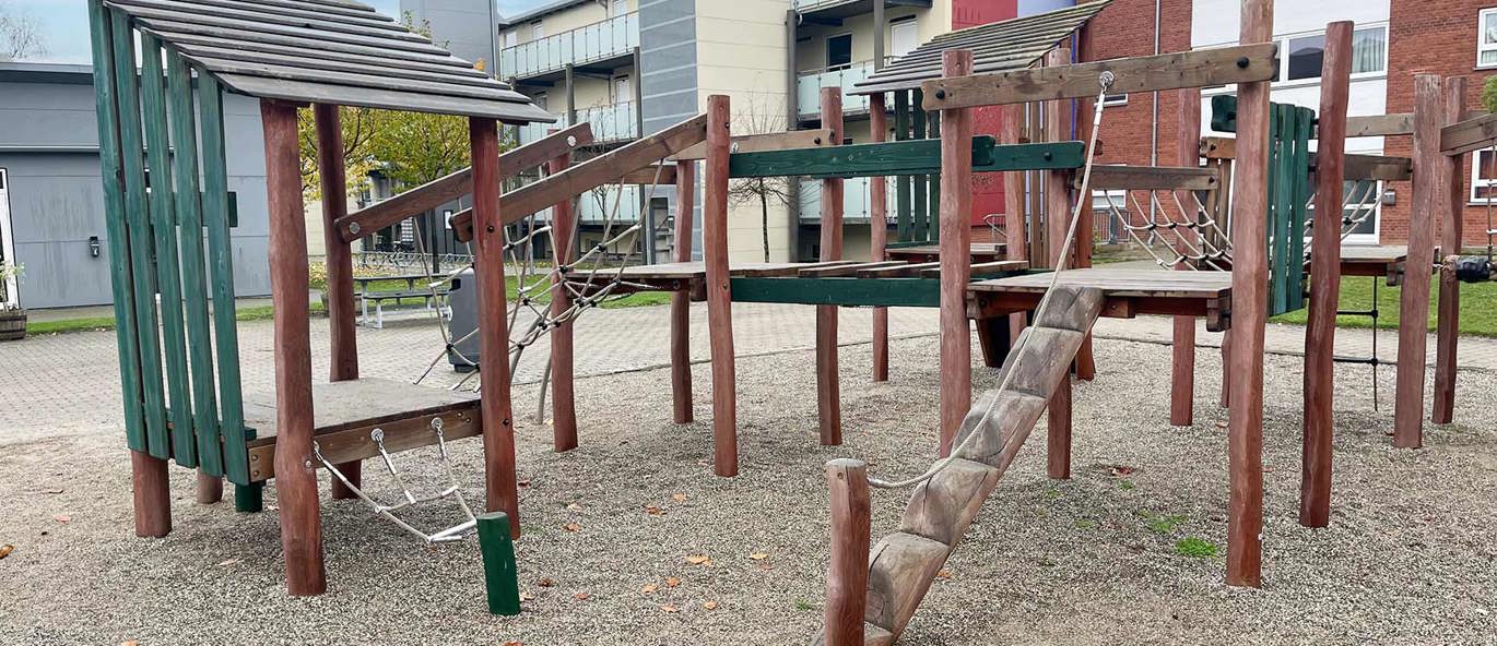 Lekeplass med klatreapparater på grusunderlag med boliger i bakgrunnen.