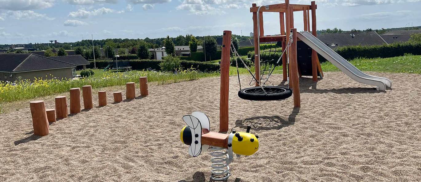 Legeplads med robinialegetårn, fugleredegynge og fjedergynge formet som bi med grøn baggrund på grusbund