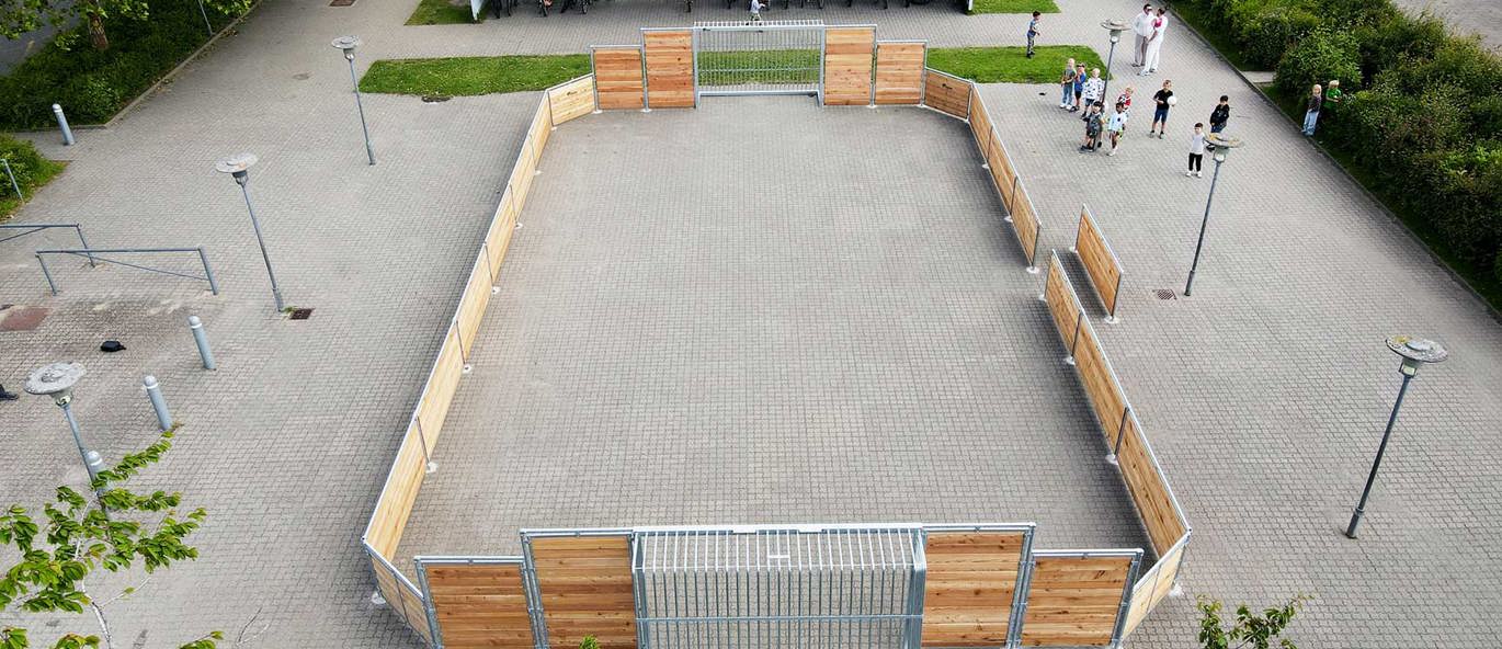 Skolegård sett ovenfra med belegningsstein og en multibane i lerk i sentrum, en annen multibane i bakgrunnen, samt et sykkelskur.