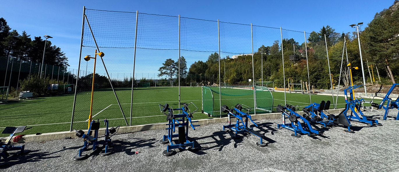 Blåa träningsmaskiner på en grusplan vid en fotbollsplan.