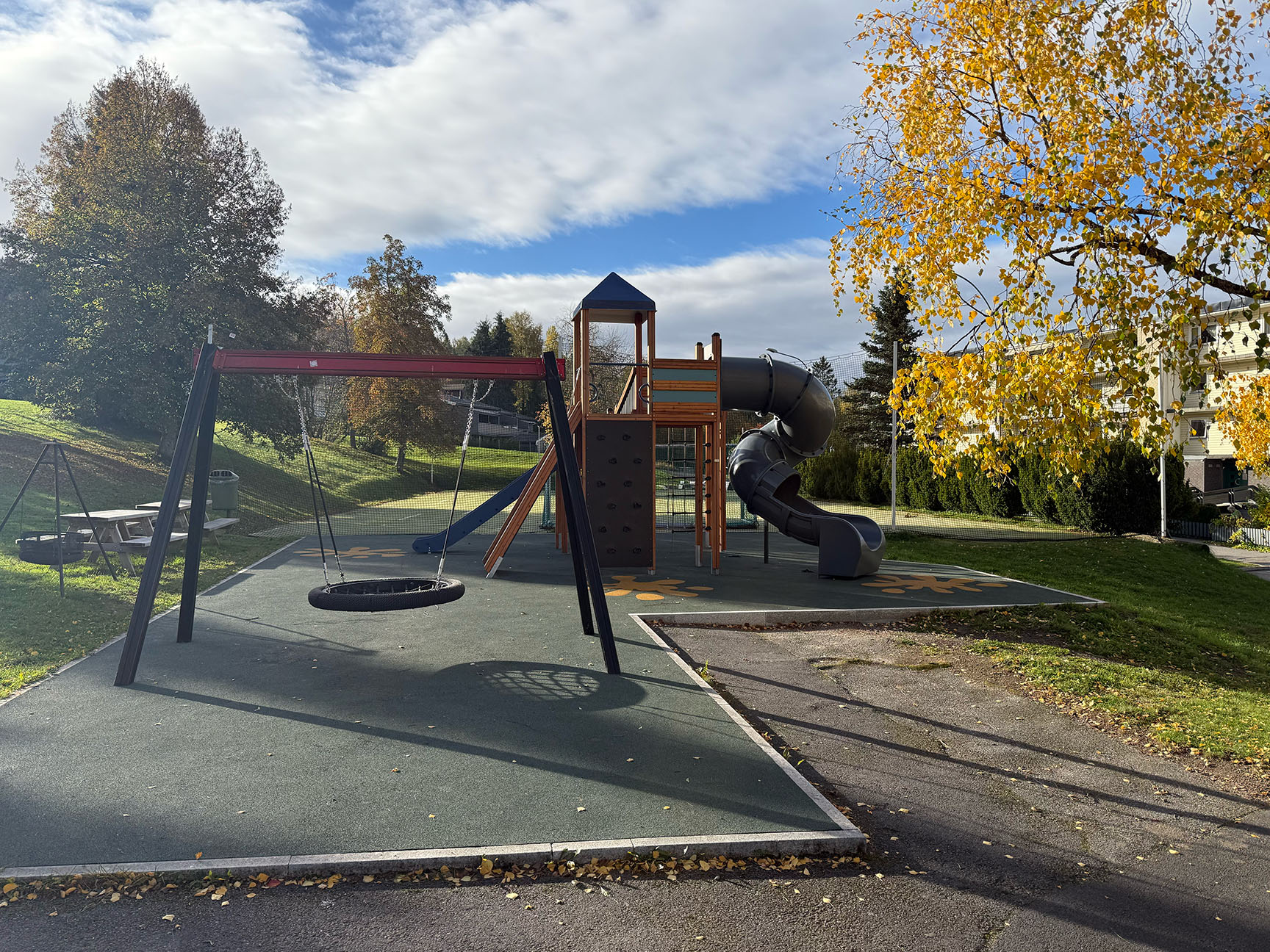 En lekplats med gungställning och hög klätterställning med skruvad rutschkana.