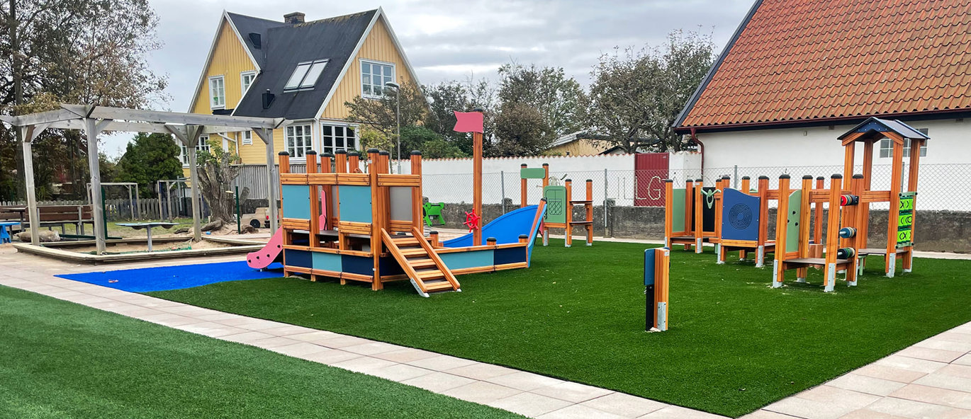 Lekplats med klätterställning och balansbana på grön och blått konstgräs.