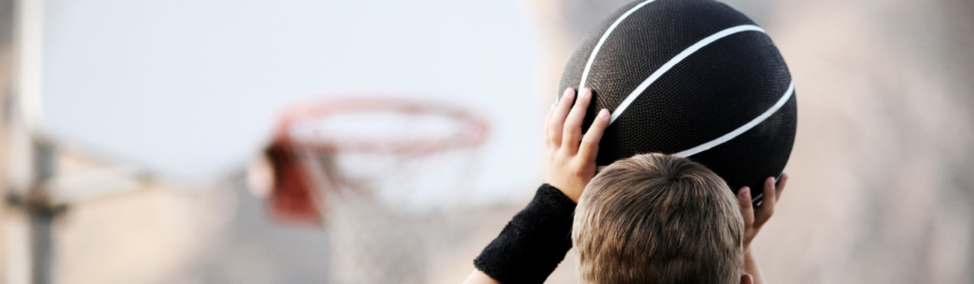 En pojke med en svart basketboll som spelar basket utomhus