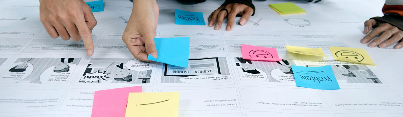 Deltagare placerar färgglada post-it-lappar på ritningar under en gemensam workshop.