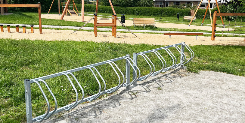 Cykelställ i galvaniserat stål med plats för flera cyklar, placerat utomhus vid en grön parkmiljö.