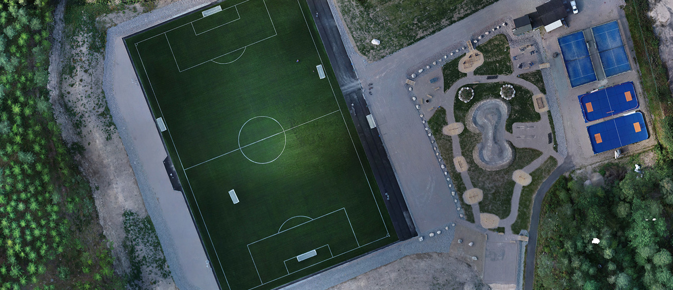 Flygvy över Ingelstads IK:s idrottsplats med ny konstgräsplan, fotbollsmål samt intilliggande aktivitetsområde och padelbanor.