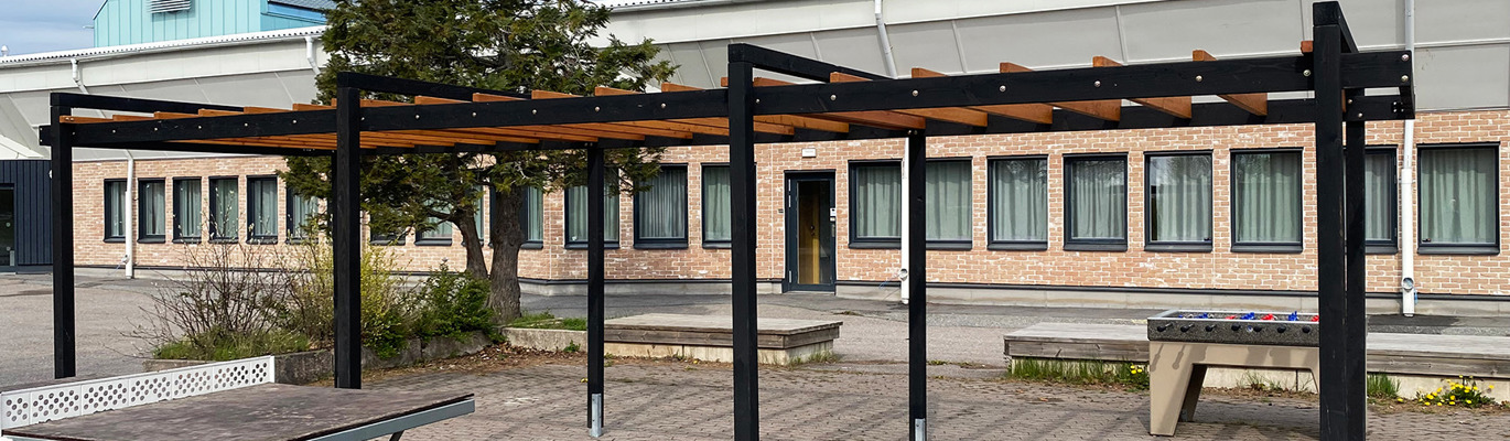 Pergola som skapar naturlig skugga över lekplats med lekställning och sandyta i bostadsmiljö.