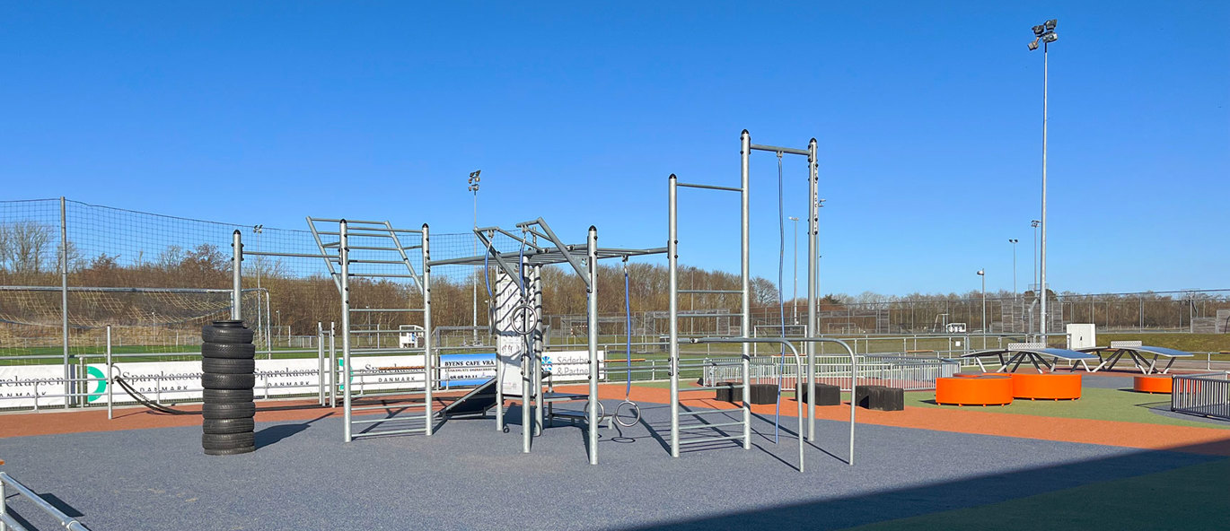 Utegym på grått underlag med orange parkmöbler i bakgrunden.