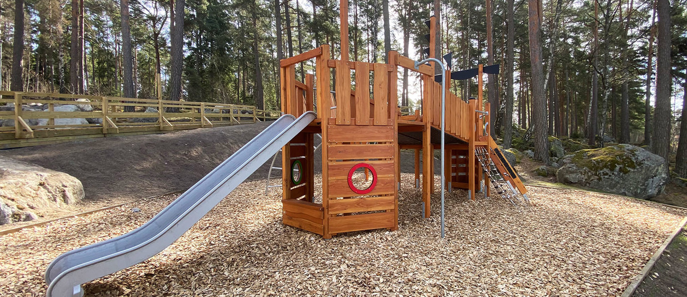 Legestruktur i træ med rutsjebane og brandmandsstang, placeret i et skovområde