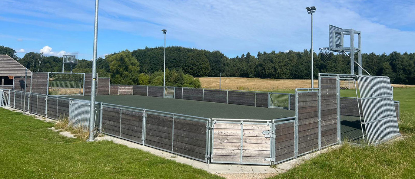 Multibane på græsplæne med lys og mål på alle sider af banen
