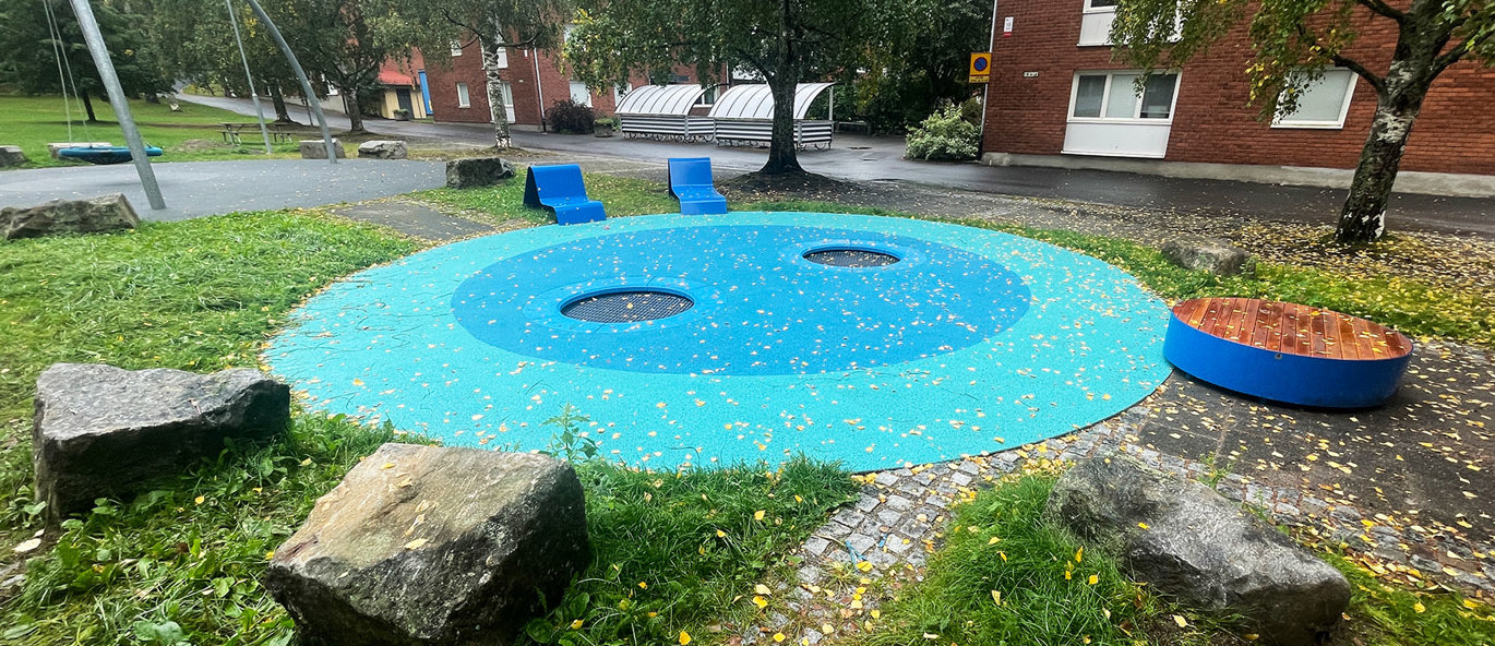 Rund gummiyta i blåa nyanser i en park med blåa stålstolar och en rund blå sittbänk.