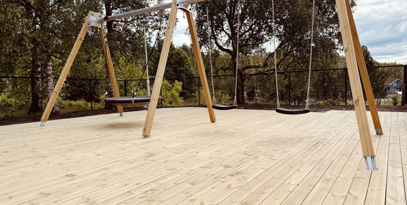 Gungställning på lekplats med trätrall och stötdämpande fallunderlag